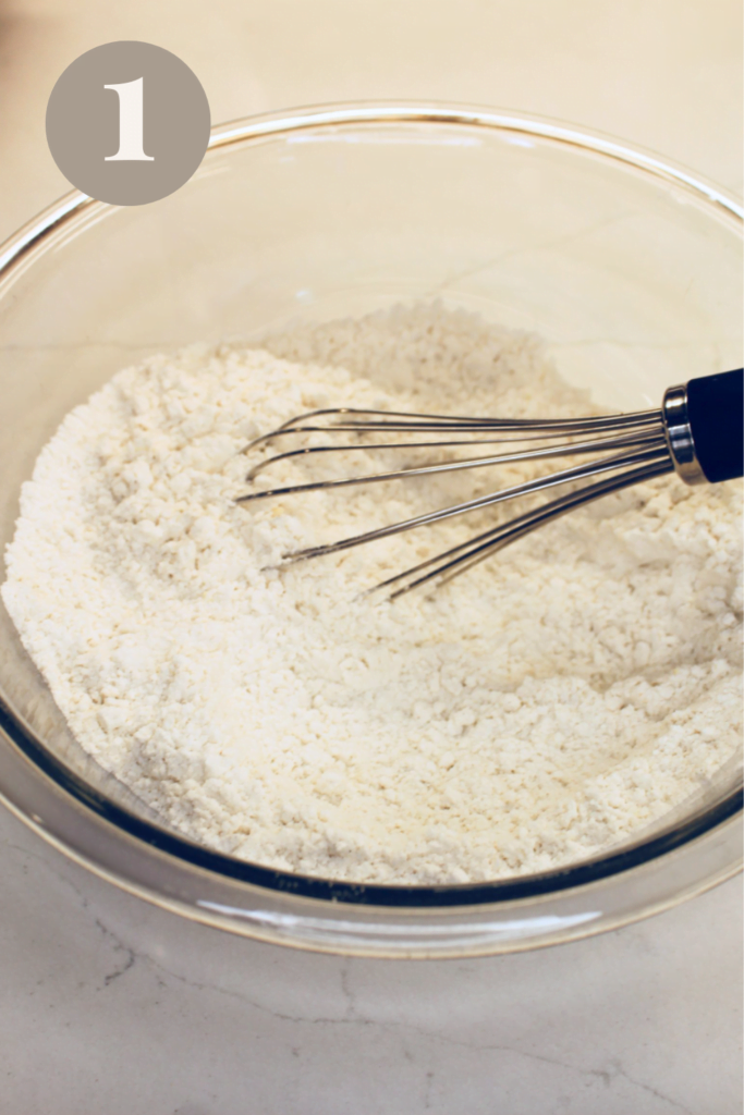 Mixed dry ingredients in a glass bowl with a whisk.