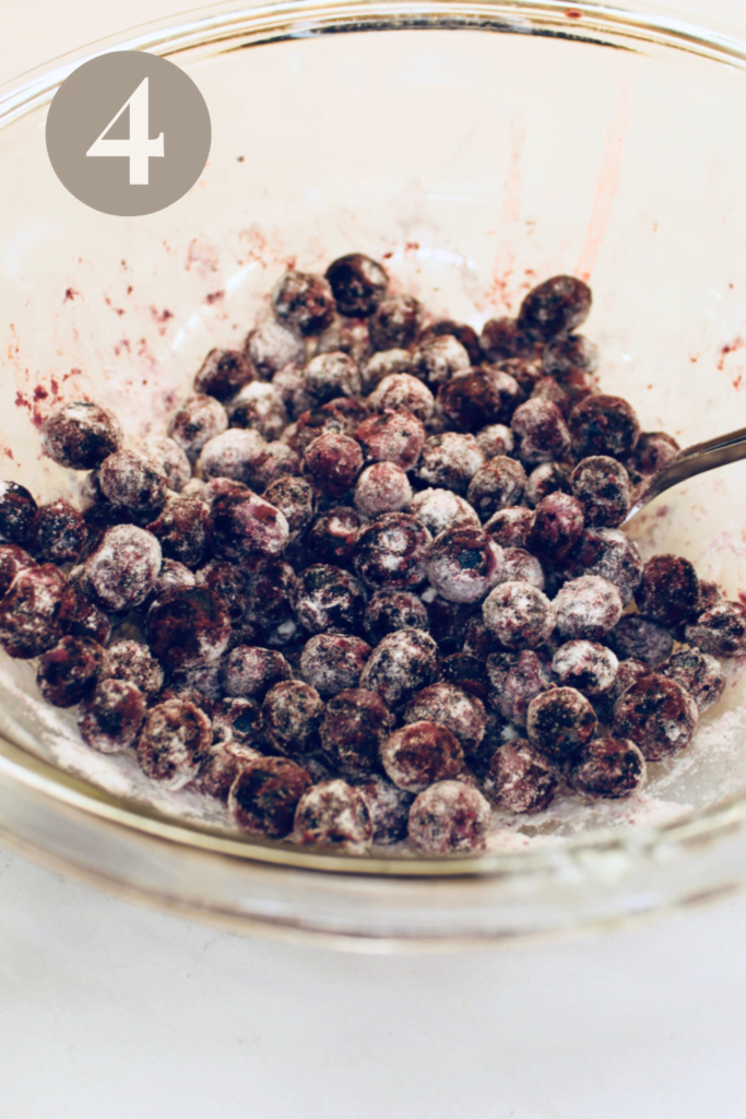 Blueberries covered in flour in a glass bowl.