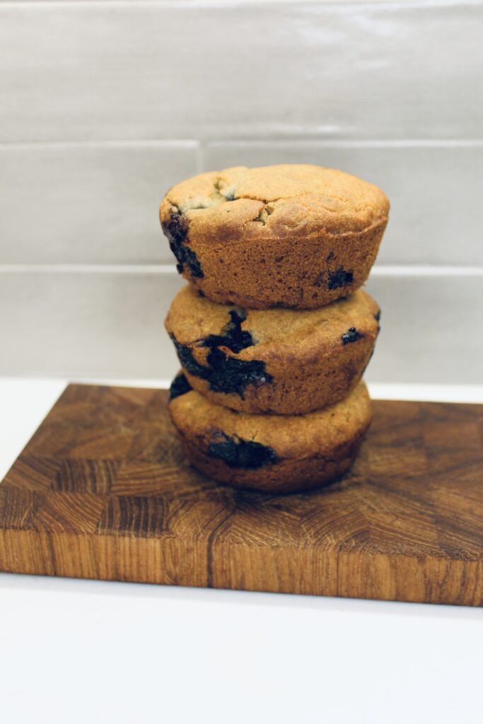 Three blueberry muffins stacked on top of each other on a cutting board.