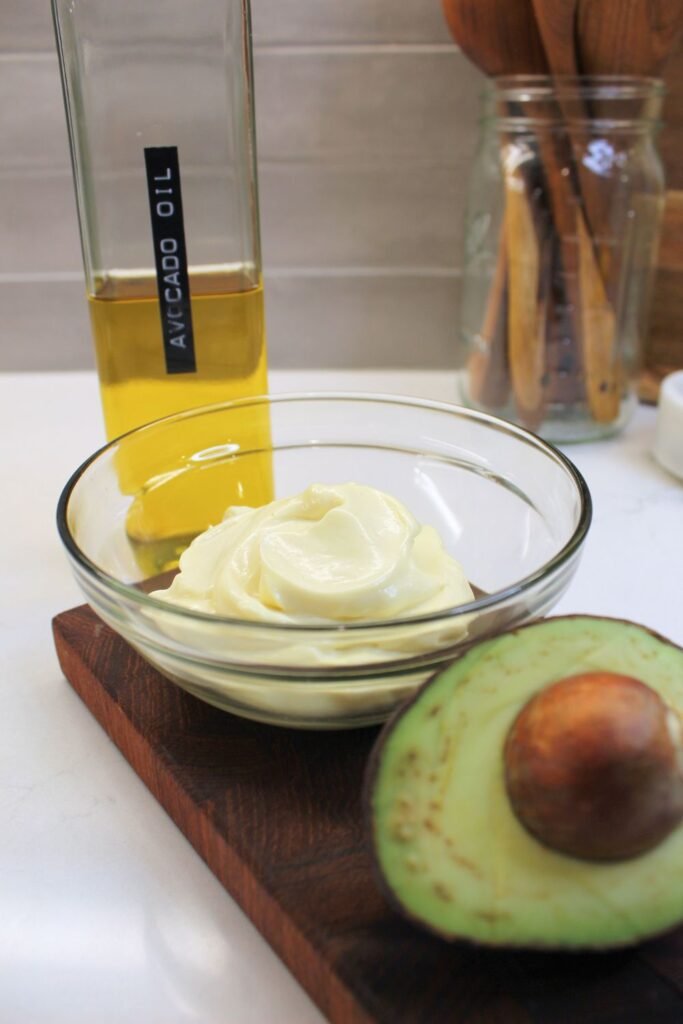 Avocado mayo in glass jar on a cutting board.