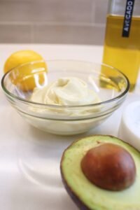 Homemade mayo in a glass bowl with oil, avocado and lemon.