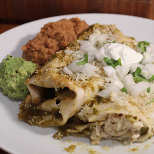 Creamy green chile enchiladas on a plate with beans and guacamole.