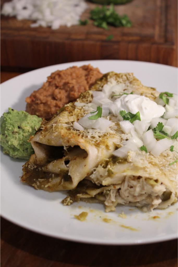 Creamy green chile enchiladas on a plate with beans and guacamole.