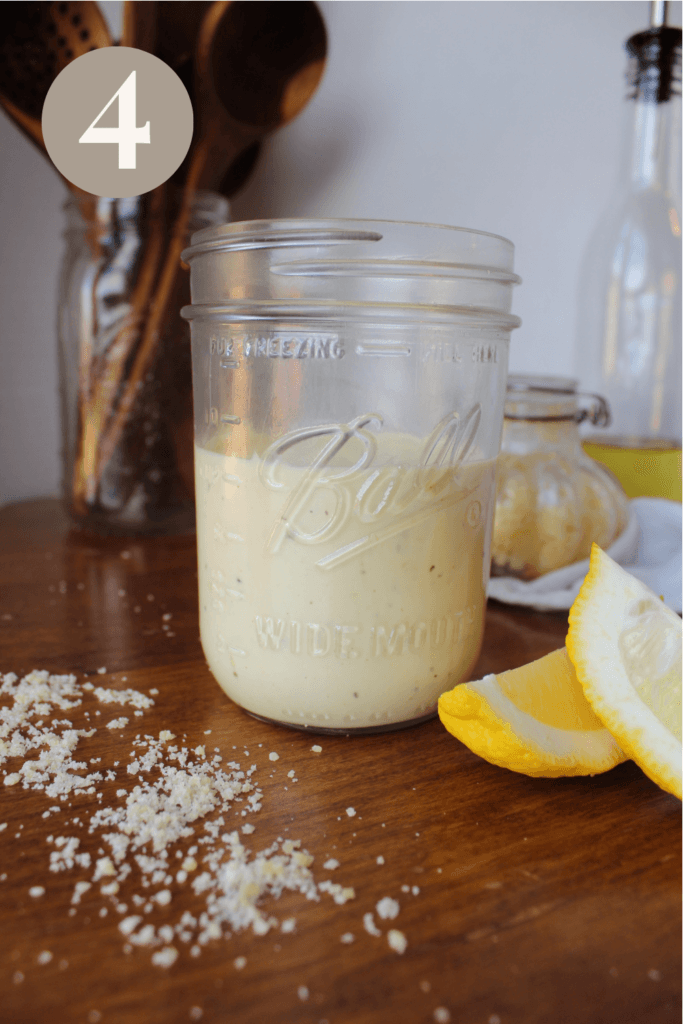 Finished caesar salad in a jar sitting on the table with lemon wedges.