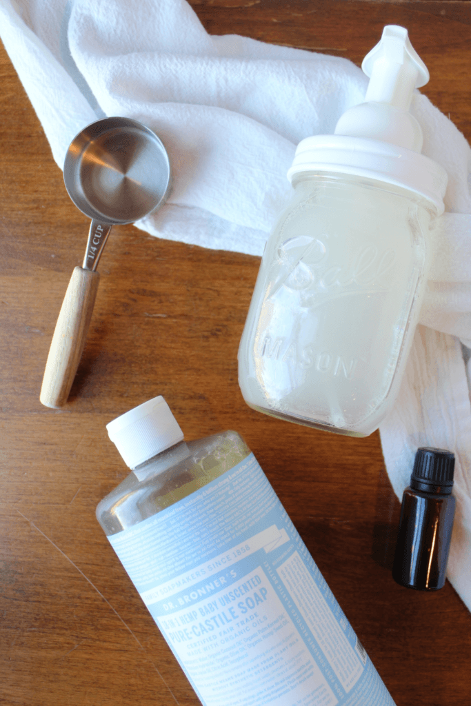 Hand soap, measuring spoon, Castile soap and essential oil on a table.