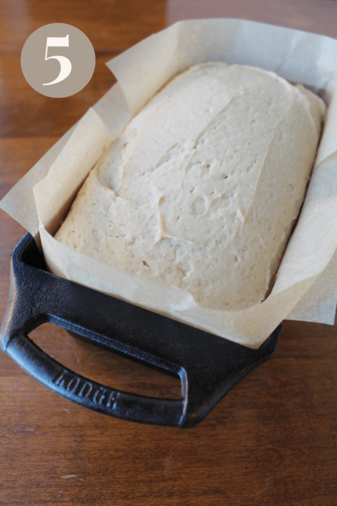 Bread has risen after proofing in a bread pan with parchment paper.