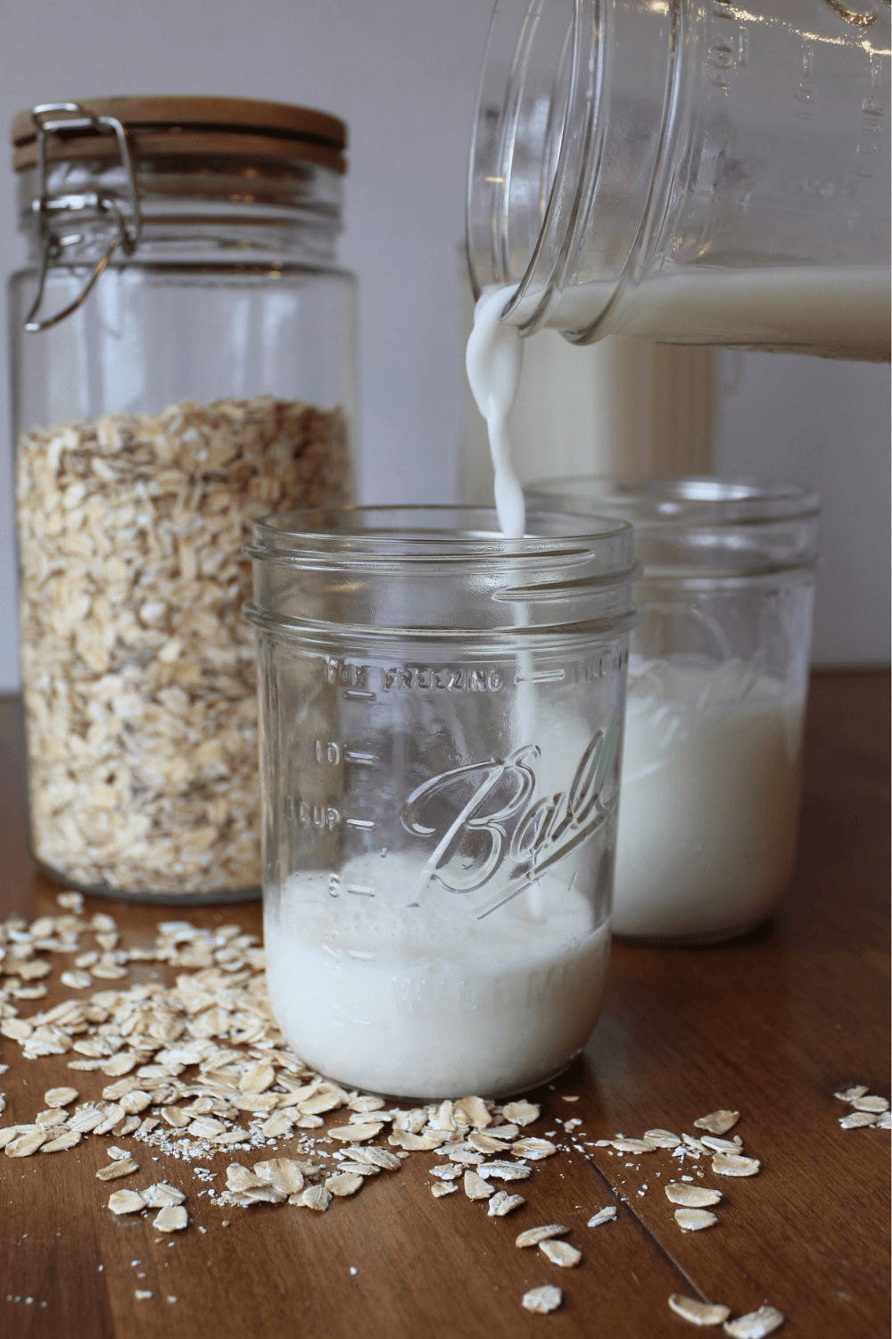 Oat milk being poured into a glass surrounded by oats on the table.