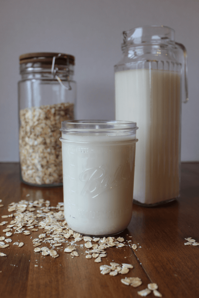 Oat milk in a glass and in a pitcher on the table with oats.