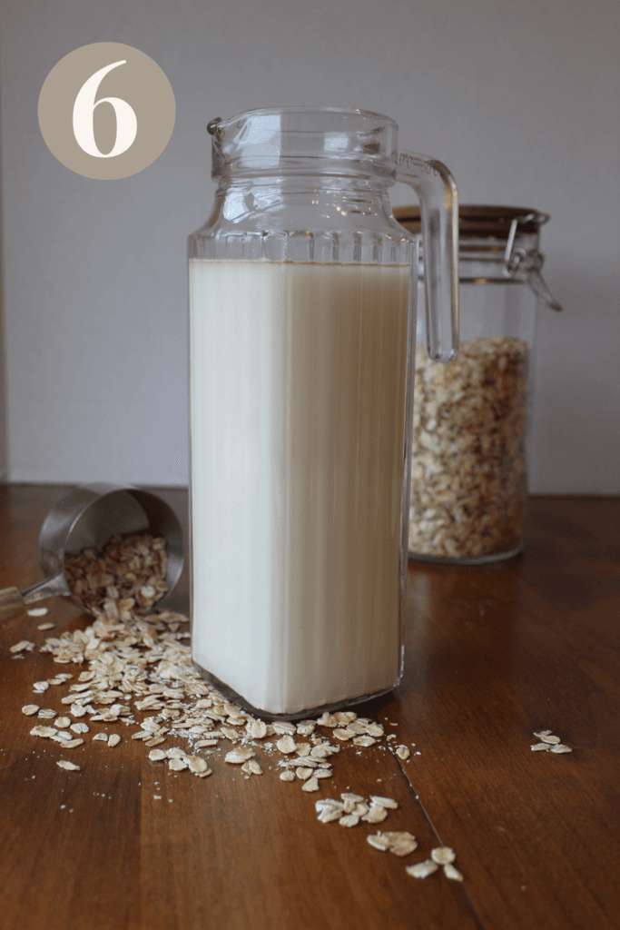 Oat milk in a glass pitcher on the counter with a jar of oats.
