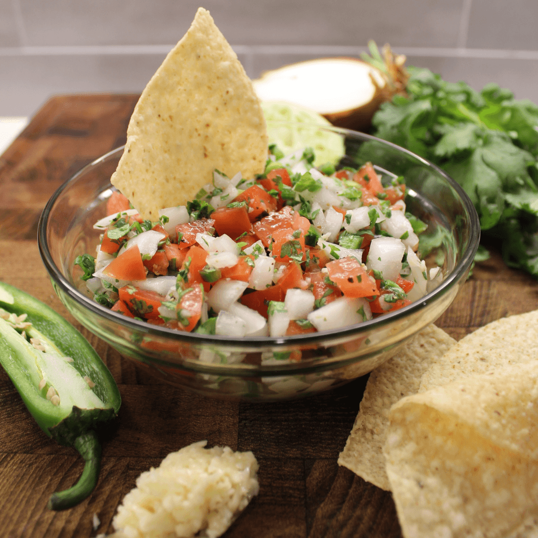 Pico de gio ion a bowl sitting on a cutting board with tortilla chips.