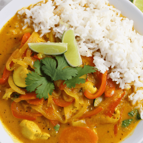 Chicken that curry in a bowl served with rice with lime and cilantro on the side of the bowl.