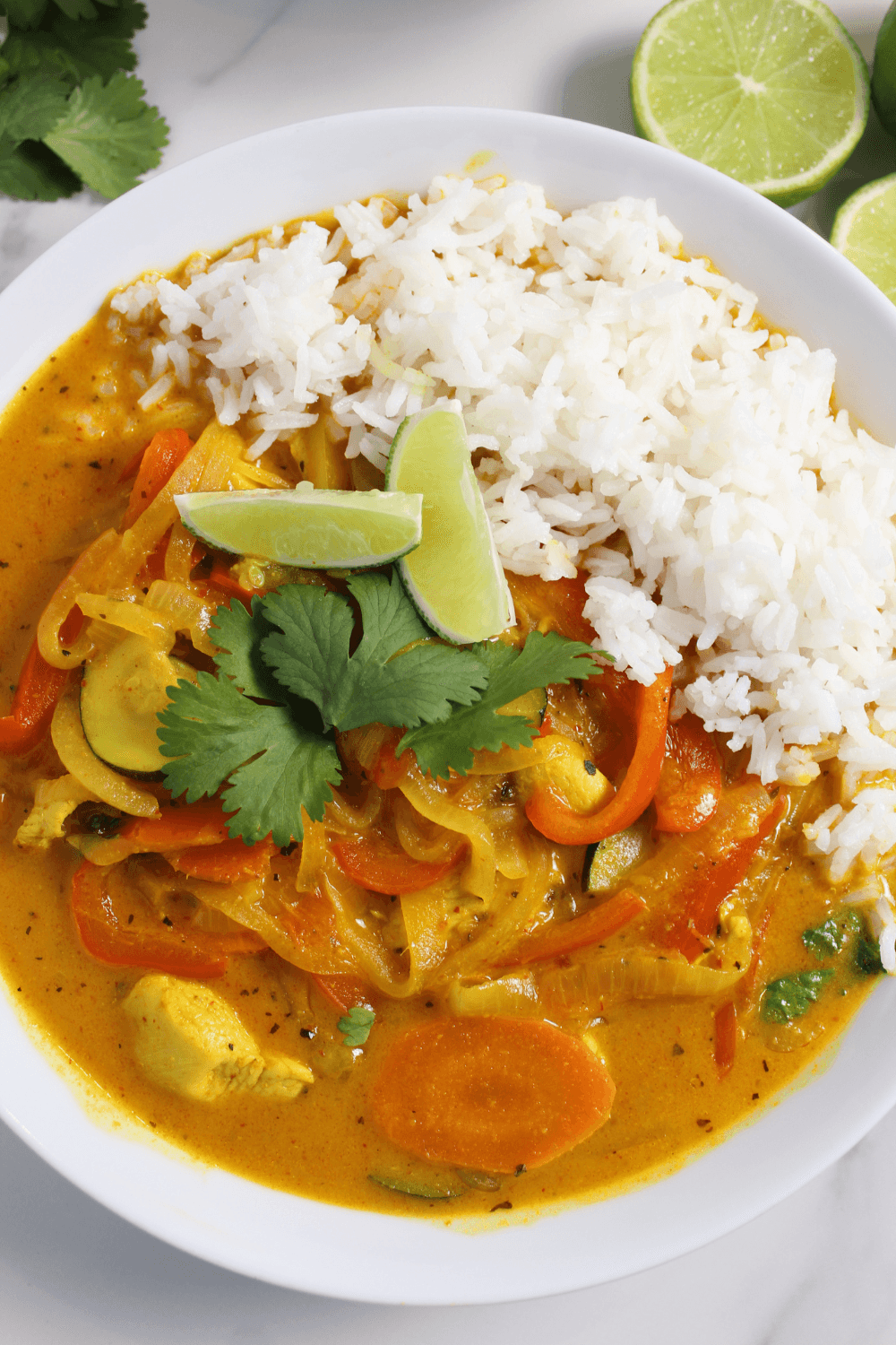 Chicken that curry in a bowl served with rice with lime and cilantro on the side of the bowl.