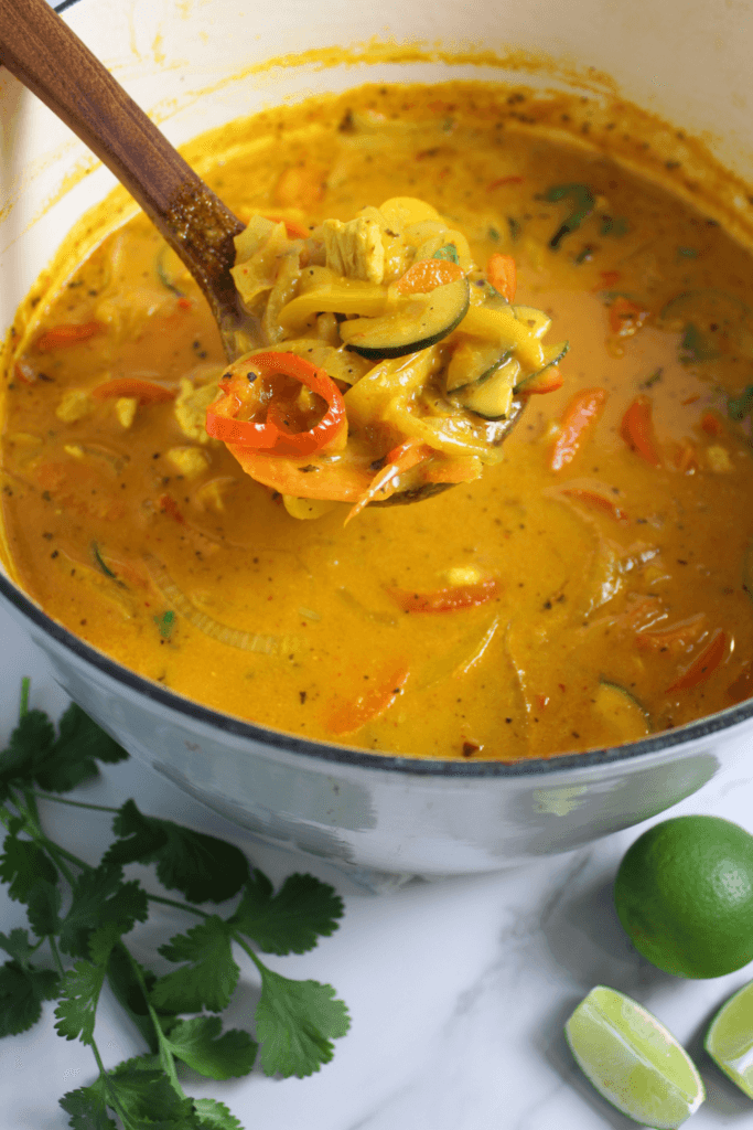 Thai red curry in a large dutch oven with a wooden laddle coming out of it.