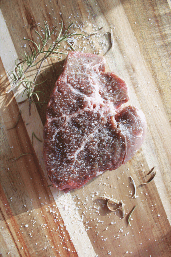 Steak salted with rosemary on a wood cutting board.