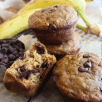 Banana bread muffins stacked on a wire rack with chocolate chips and bananas.