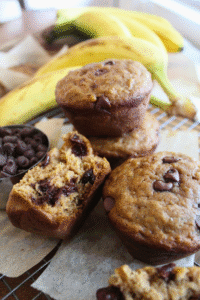 Banana bread muffins stacked on a wire rack with chocolate chips and bananas.