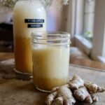 Ginger bug soda in a glass next to some ginger on a wood table.