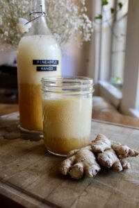 Ginger bug soda in a glass next to some ginger on a wood table.