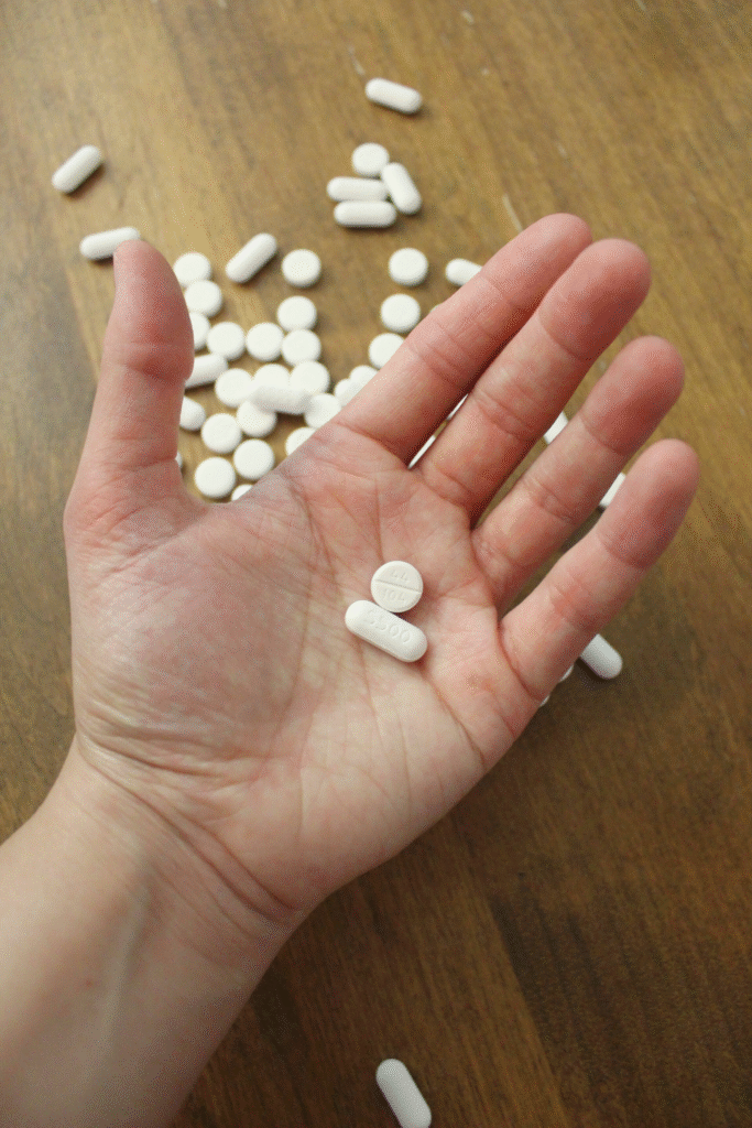 Pain reliever pills in a hand above more pills on the table.