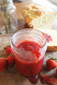 Strawberry honey jam sitting on a wood cutting board with strawberries and einkorn bread.