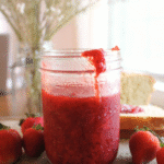 Strawberry honey jam sitting on a wood cutting board with strawberries.