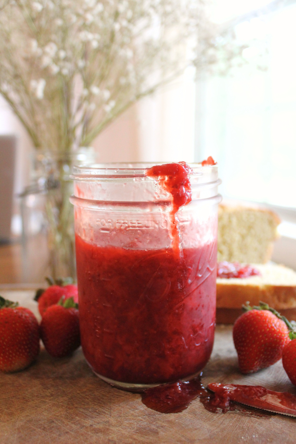 Strawberry honey jam sitting on a wood cutting board with strawberries.